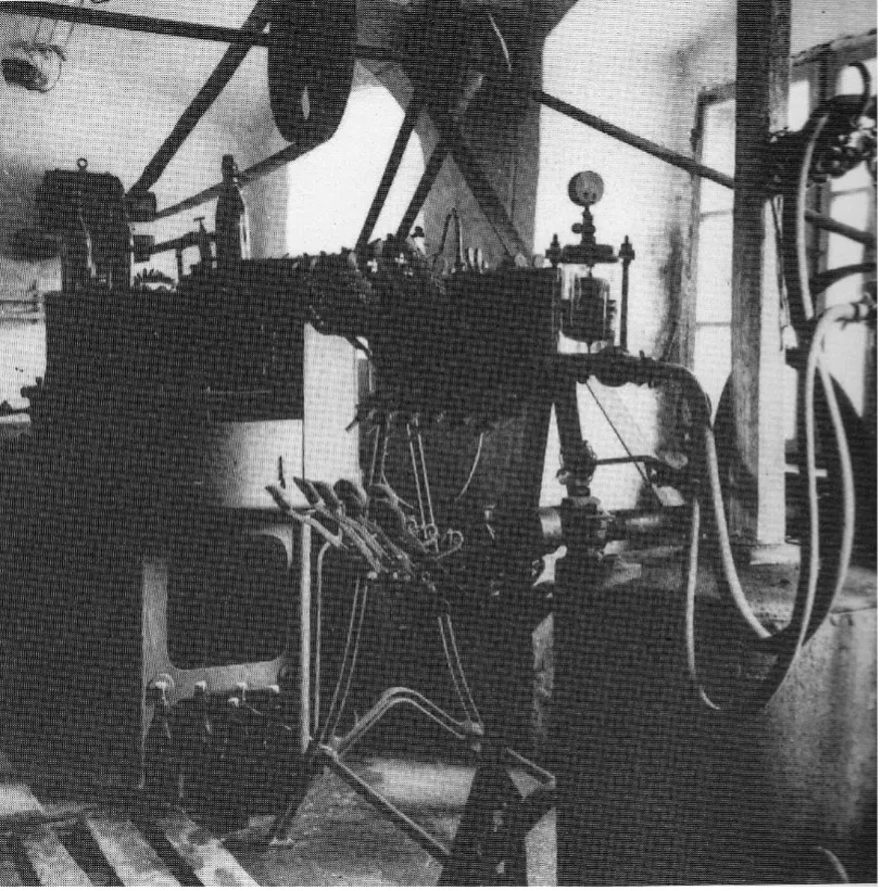 Schwarz-Weiß-Foto einer alten Industriemaschine mit Messgeräten, Rohren und Hebeln in einer Werkstatt.