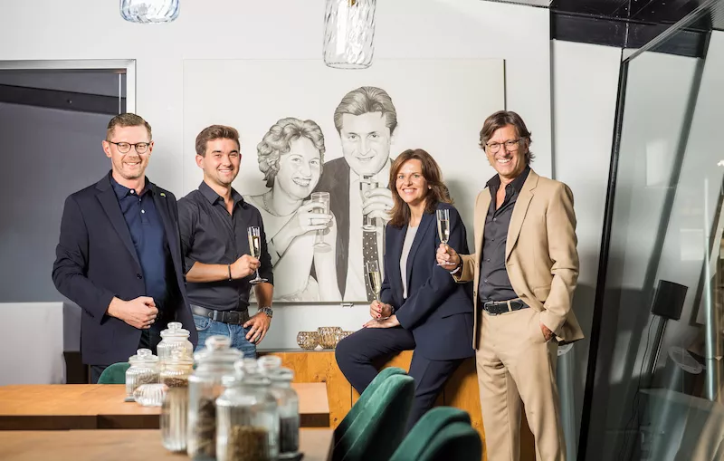 Vier Personen aus dem Familienunternehmen Kunzmann stehen in einem modernen, stilvoll eingerichteten Raum und halten Sektgläser in der Hand.