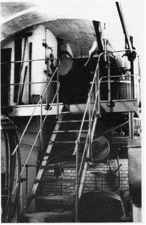 Schwarz-Weiß-Foto des Brauerei Sudhauses 1933, mit einer Treppe, die zu einer Plattform führt, Geländern entlang der Treppe und großen zylindrischen Tanks im Hintergrund